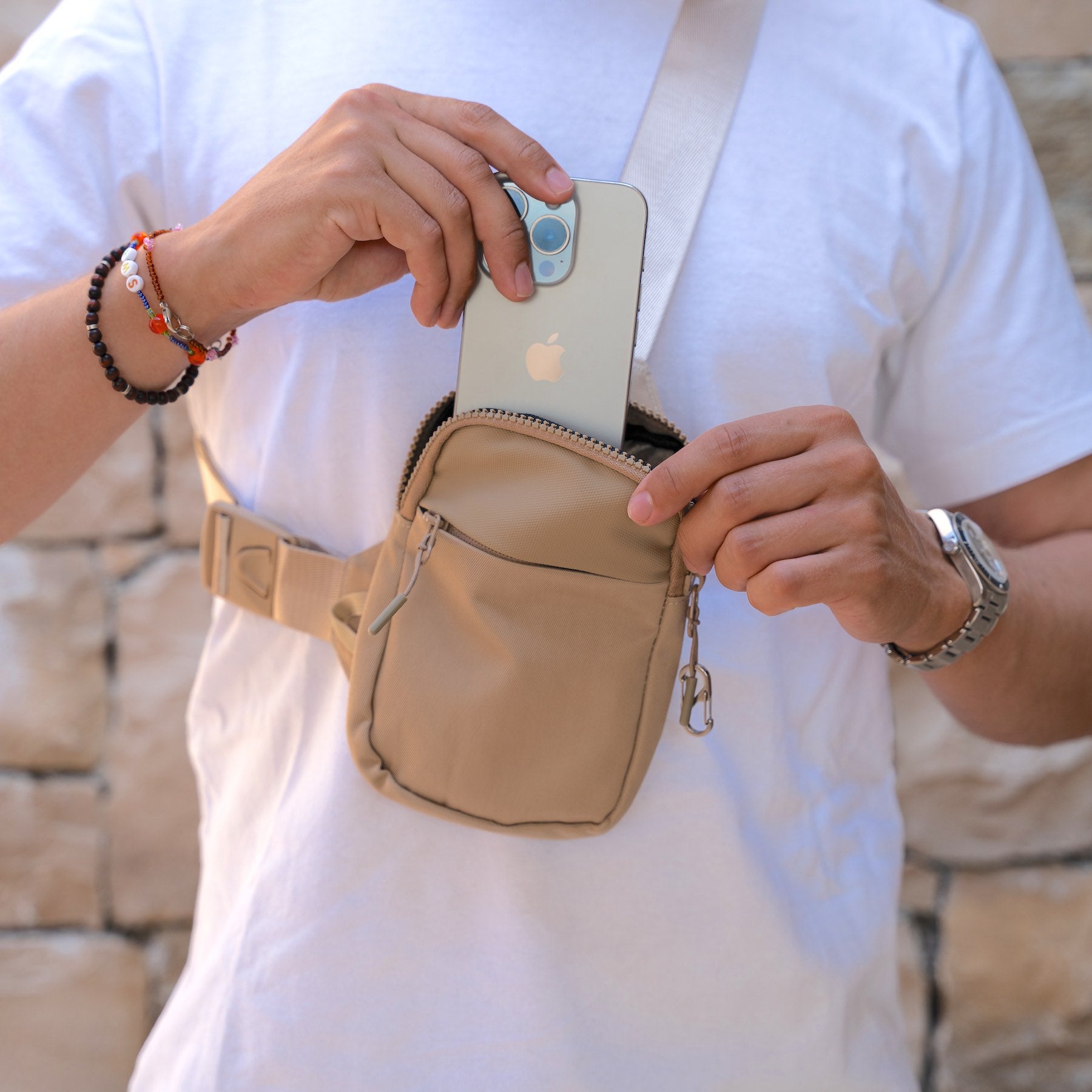 Person holding a beige waist bag with an Apple phone inside, wearing a white shirt.