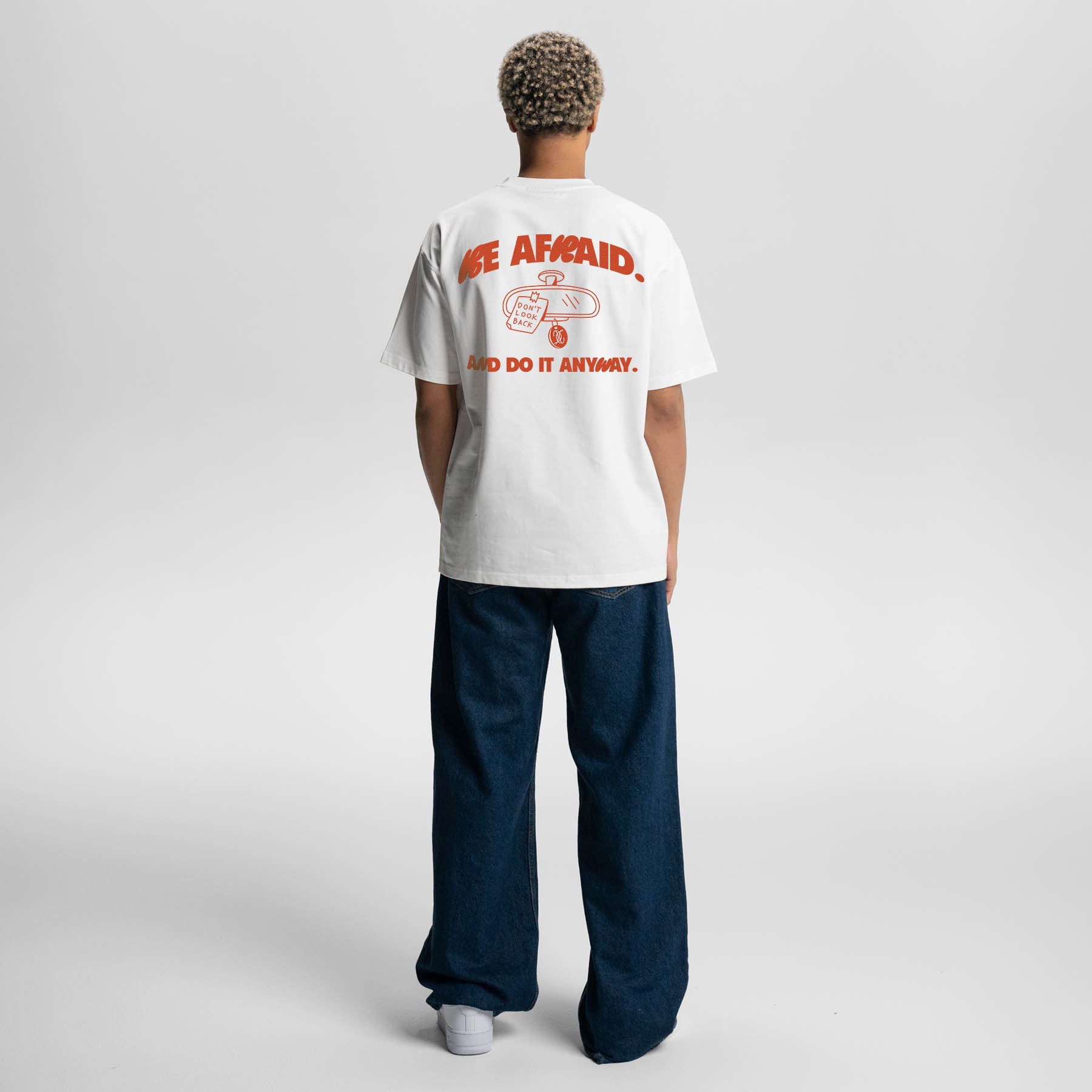 Person wearing a white t-shirt with red text and graphics on the back, standing against a plain background.